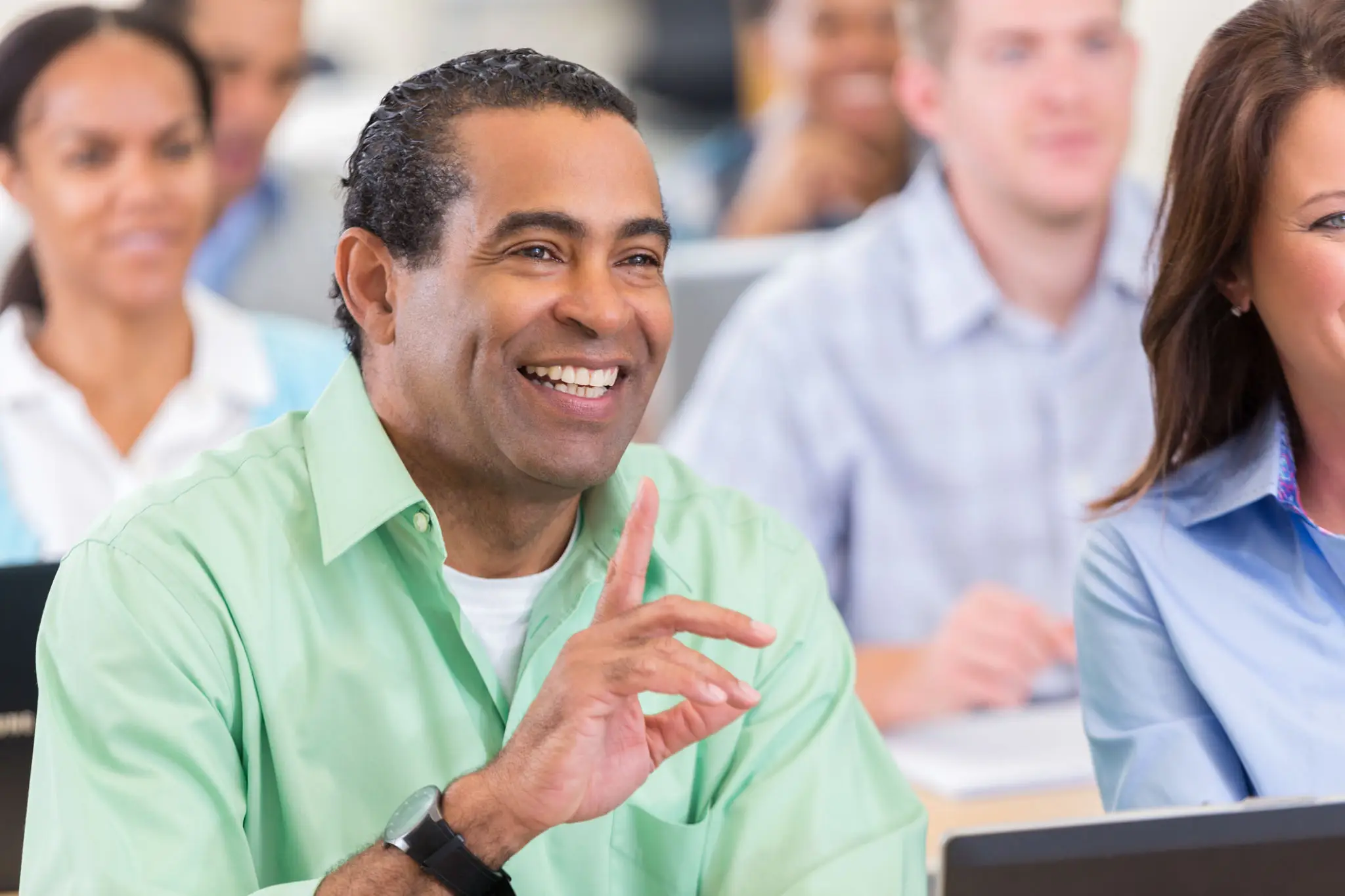 A smiling man raising his hand in a classroom setting.