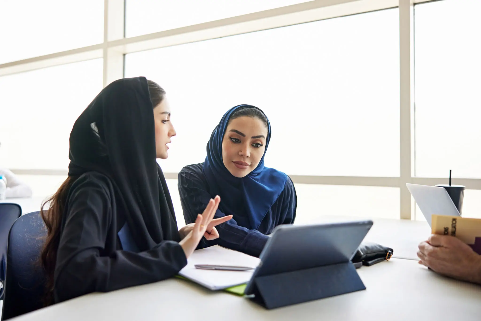 Two women in hijabs working together on a tablet.